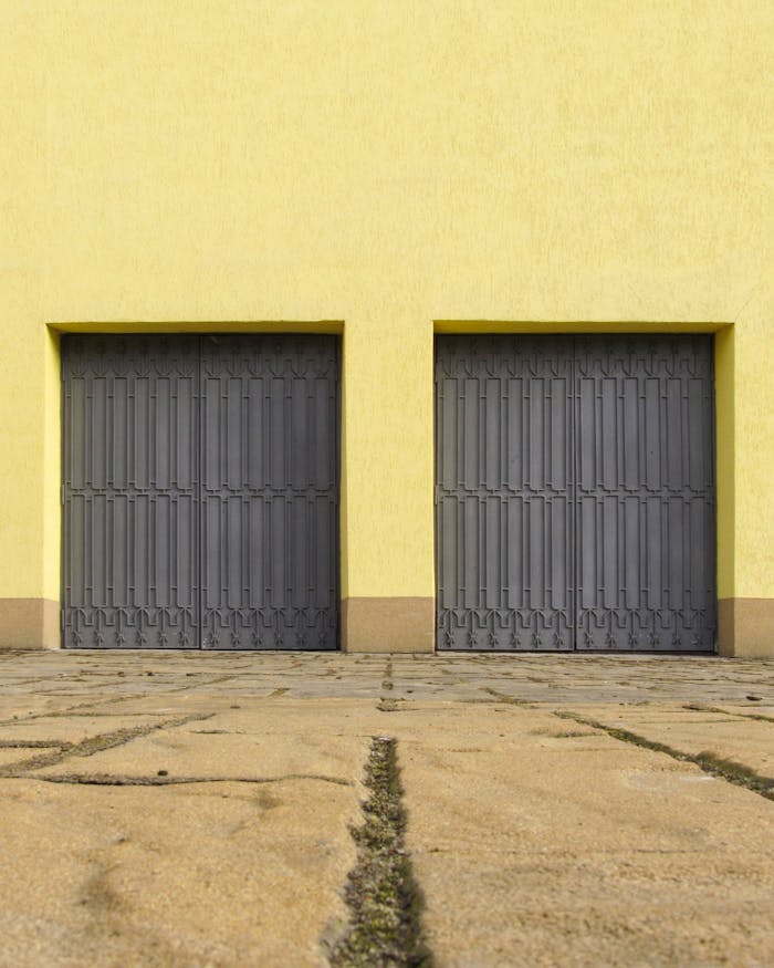 Yellow wall with two closed grey garage doors creates a minimalist urban scene. Ideal for architecture and design concepts.
